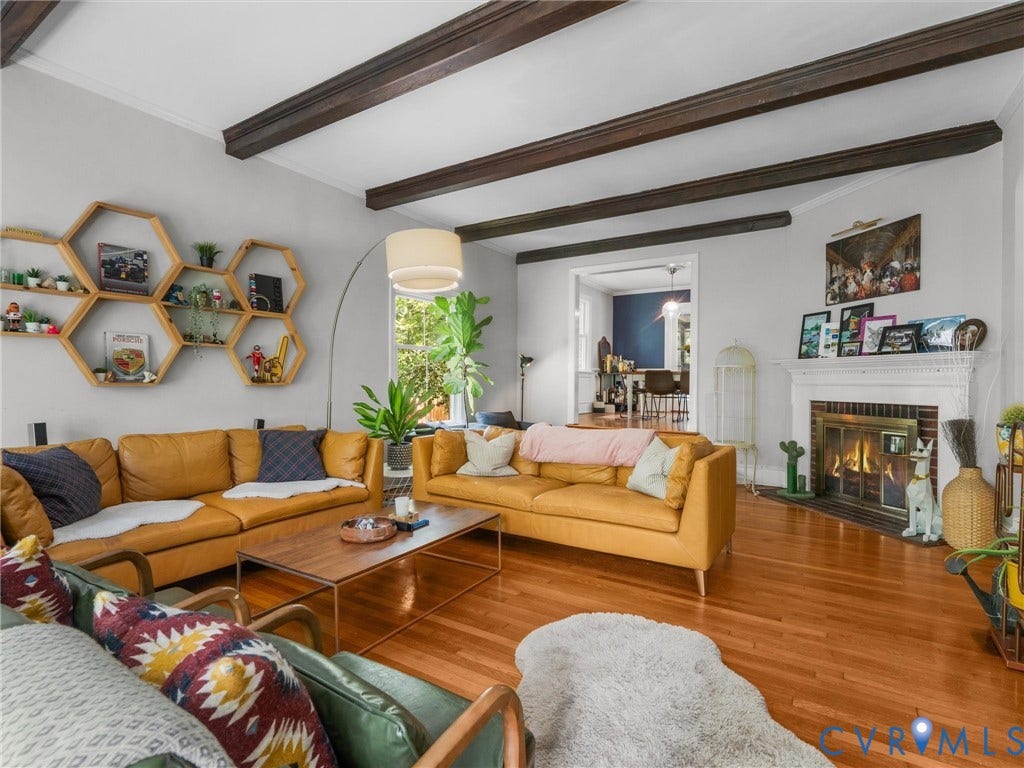 Exposed wood beam ceiling, wood-finish flooring, built-in fireplace with a decorative mantel, and recessed window