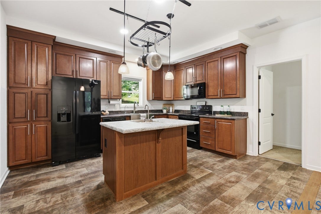 2575 Log Cabin Road, Maidens, VA 23102 Kitchen featuring wood-finish LVP flooring, wood cabinetry, black appliances, a central island with a light-toned countertop, and a pot rack.