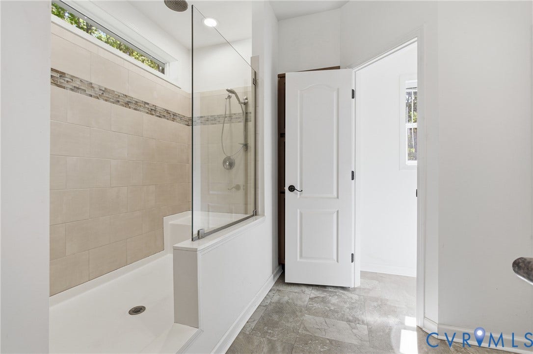 2575 Log Cabin Road, Maidens, VA 23102 Frameless glass shower featuring ceiling-mounted rain showerhead, handheld shower wand, built-in seating, transom window for natural light and decorative accent tile.