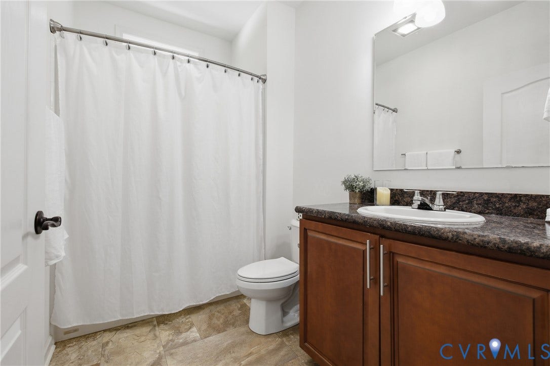 2575 Log Cabin Road, Maidens, VA 23102 Vanity with a built-in sink, dark countertop, and wood-finish cabinetry with silver-tone hardware. Tub shower combo with a transom window for natural light and decorative accent tile.