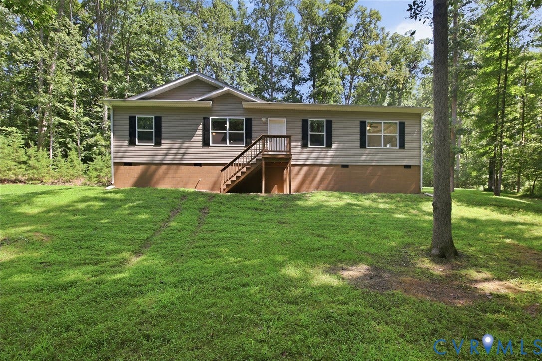 2575 Log Cabin Road, Maidens, VA 23102 Siding exterior with black window shutters, elevated wooden deck, and a surrounding wooded landscape