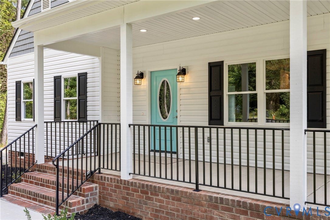 Covered front porch featuring white siding, black shutters, brick foundation, and metal railings