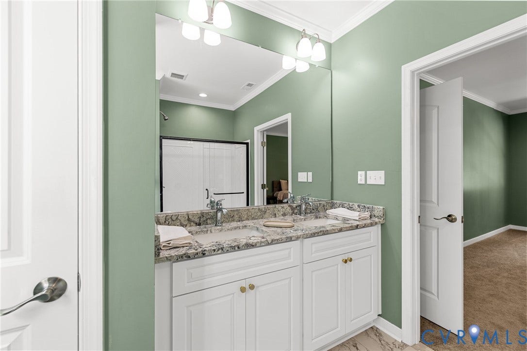 Double vanity with granite countertop and integrated sinks, white cabinetry, tiled flooring and a glass-enclosed shower with sliding doors