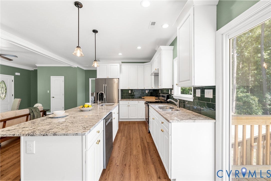 Expansive kitchen island with a light-toned countertop, white cabinetry with gold-finish hardware, stainless steel appliances, and Laminate flooring