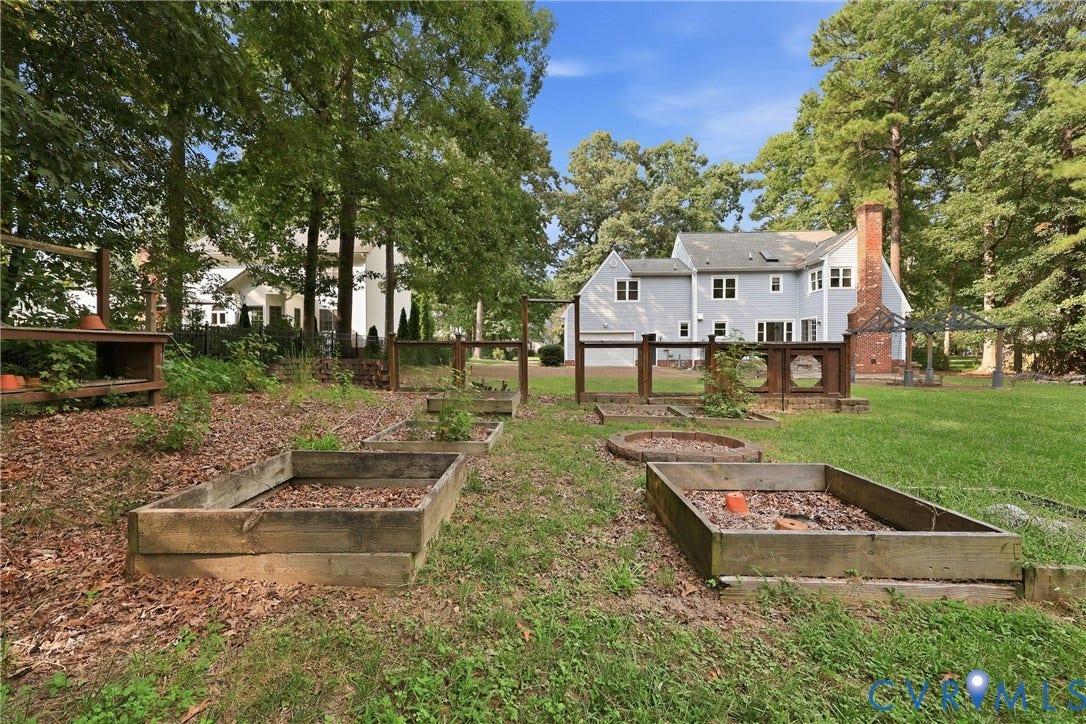 505 Martineau Drive, Chesterfield, VA 23836 Expansive backyard featuring a large lawn, multiple raised garden beds, a brick chimney, and mature trees