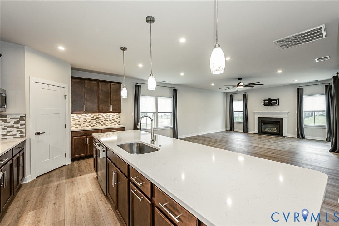 7683 Autumn Leaves Lane, Estates The Groves At New Kent, New Kent, VA 23124 Open-concept kitchen and living area featuring a large island with sink, wood-finish flooring, recessed lighting, and a fireplace with mantle