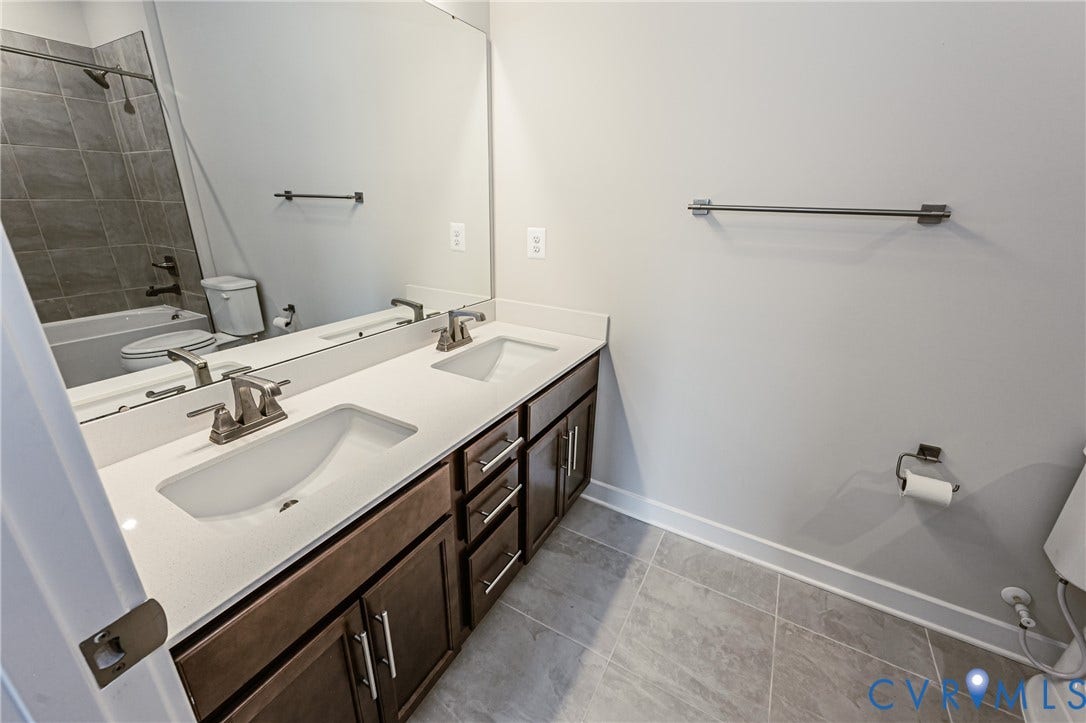 7683 Autumn Leaves Lane, Estates The Groves At New Kent, New Kent, VA 23124 Dual vanity with undermount sinks and brushed nickel faucets, dark wood-finish cabinetry with silver hardware, white countertop, large wall-mounted mirror, and tile flooring