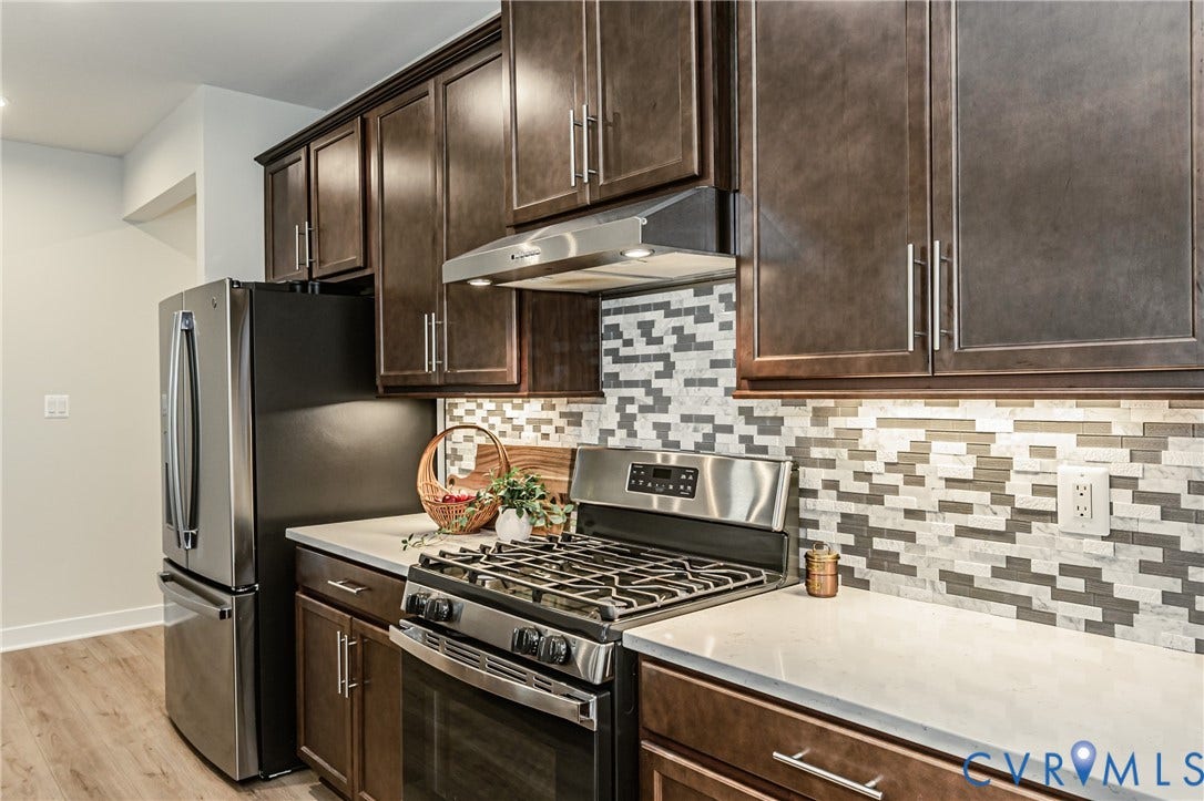 7683 Autumn Leaves Lane, Estates The Groves At New Kent, New Kent, VA 23124 Dark wood-finish cabinetry with brushed nickel hardware, stainless steel range with hood, mosaic tile backsplash, light-toned countertops, and wood-finish flooring