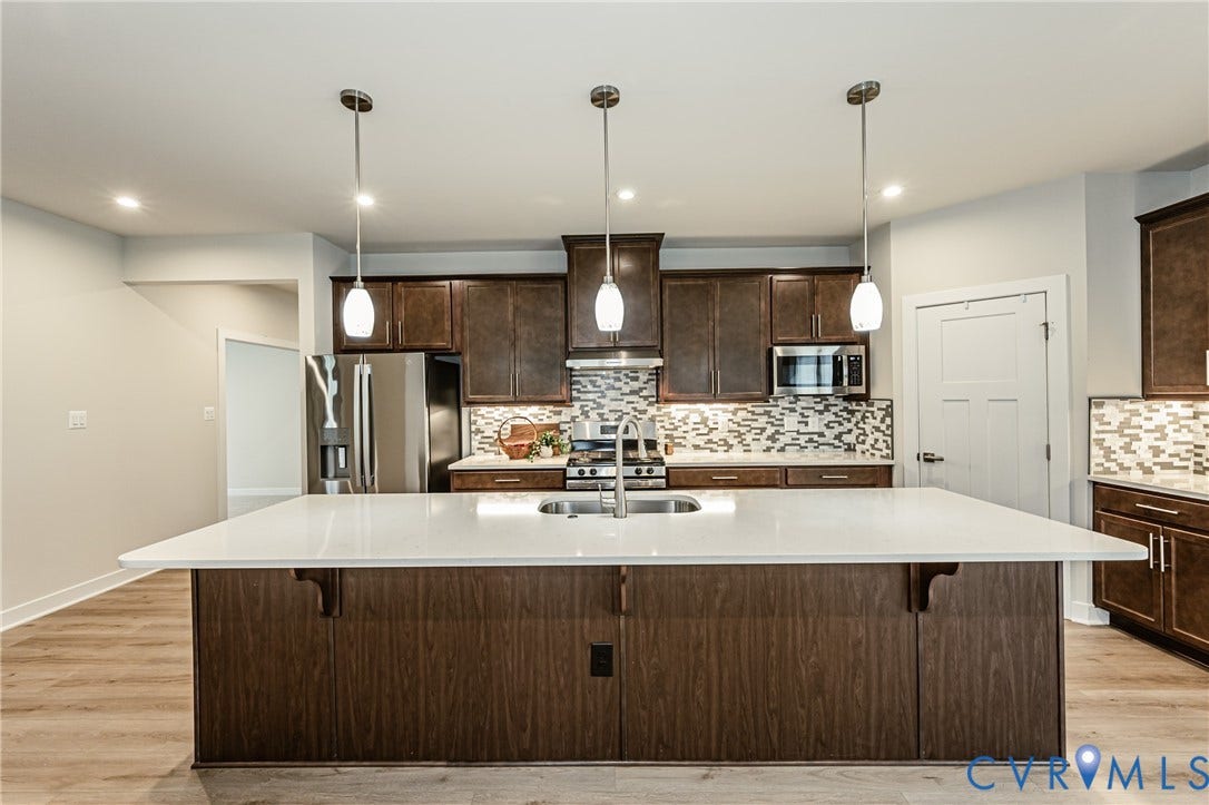 7683 Autumn Leaves Lane, Estates The Groves At New Kent, New Kent, VA 23124 Kitchen island with a light-colored countertop, dark wood-finish cabinetry, stainless steel appliances, and pendant lighting