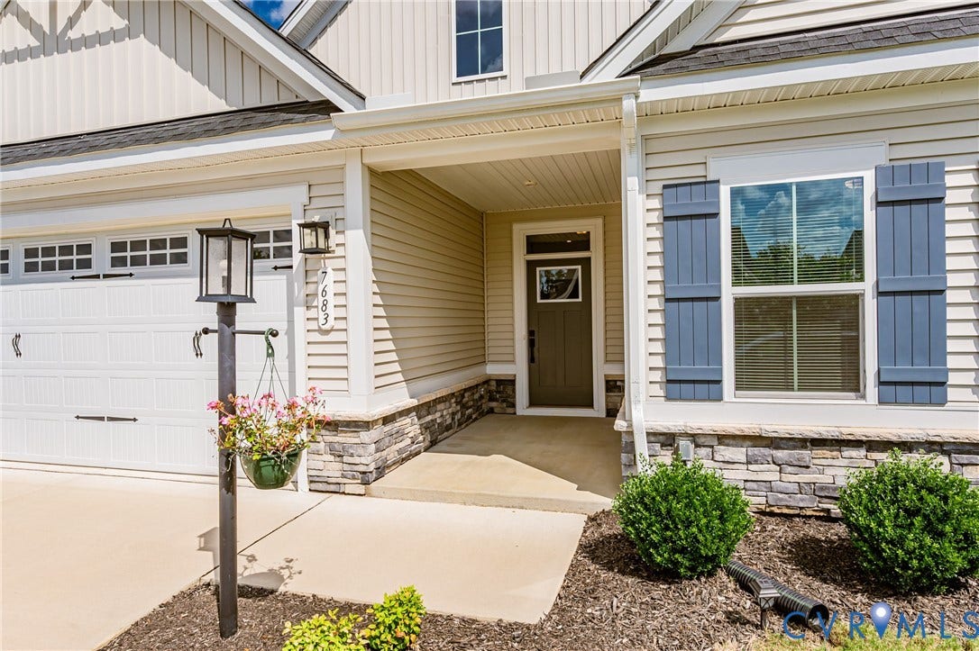 7683 Autumn Leaves Lane, Estates The Groves At New Kent, New Kent, VA 23124 Exterior featuring vinyl siding, stone veneer accents, a covered entry, a garage door with window inserts, and blue window shutters