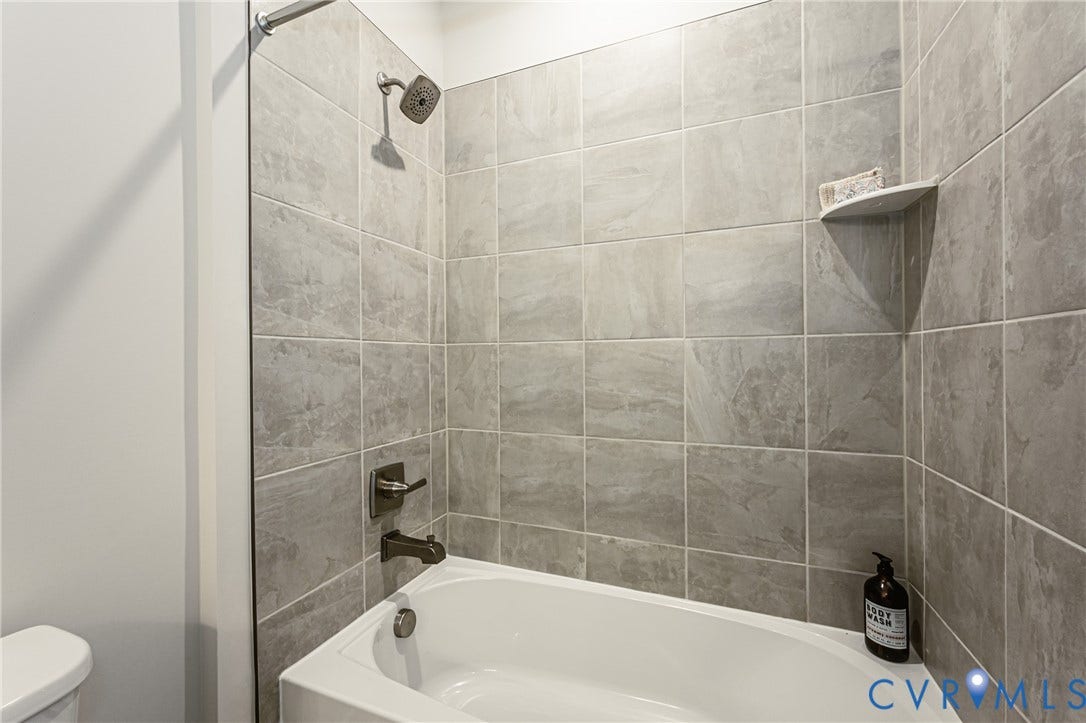 7683 Autumn Leaves Lane, Estates The Groves At New Kent, New Kent, VA 23124 White bathtub with brushed nickel fixtures, light gray large format wall tile, and a corner shelf