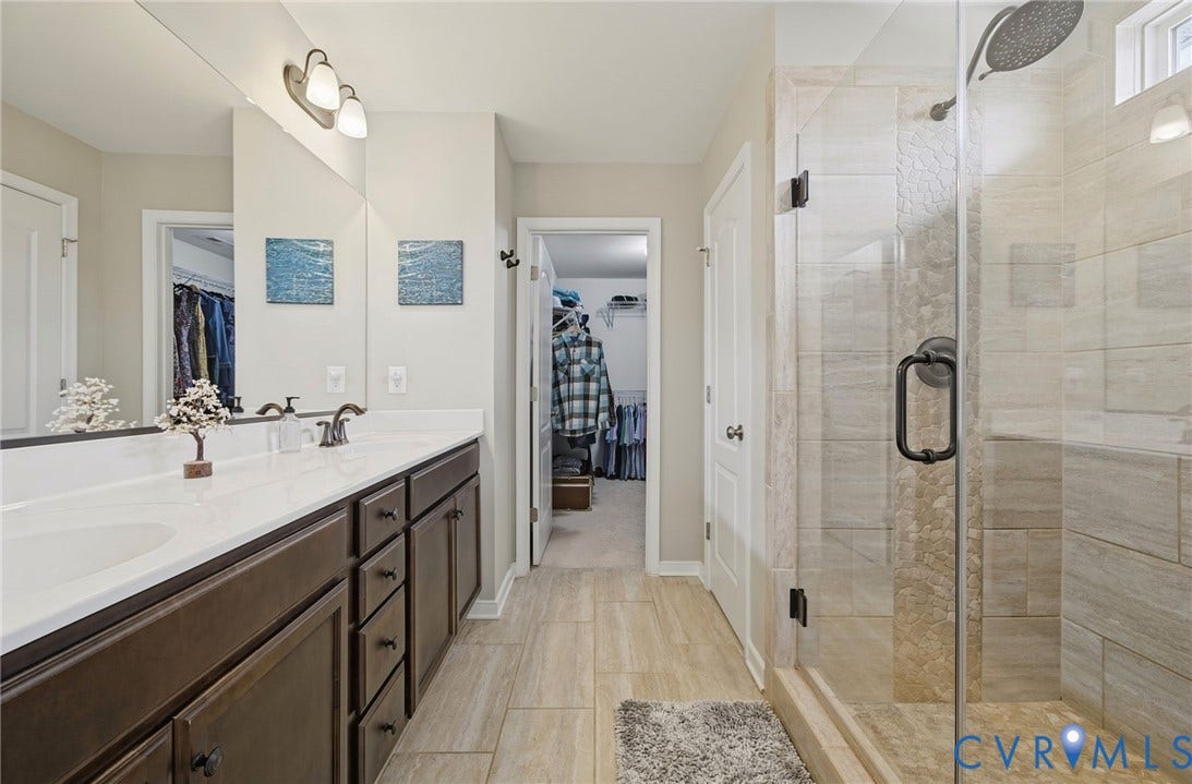 Dual vanity with integrated sinks, frameless glass shower enclosure, and tiled shower surround with pebble accent