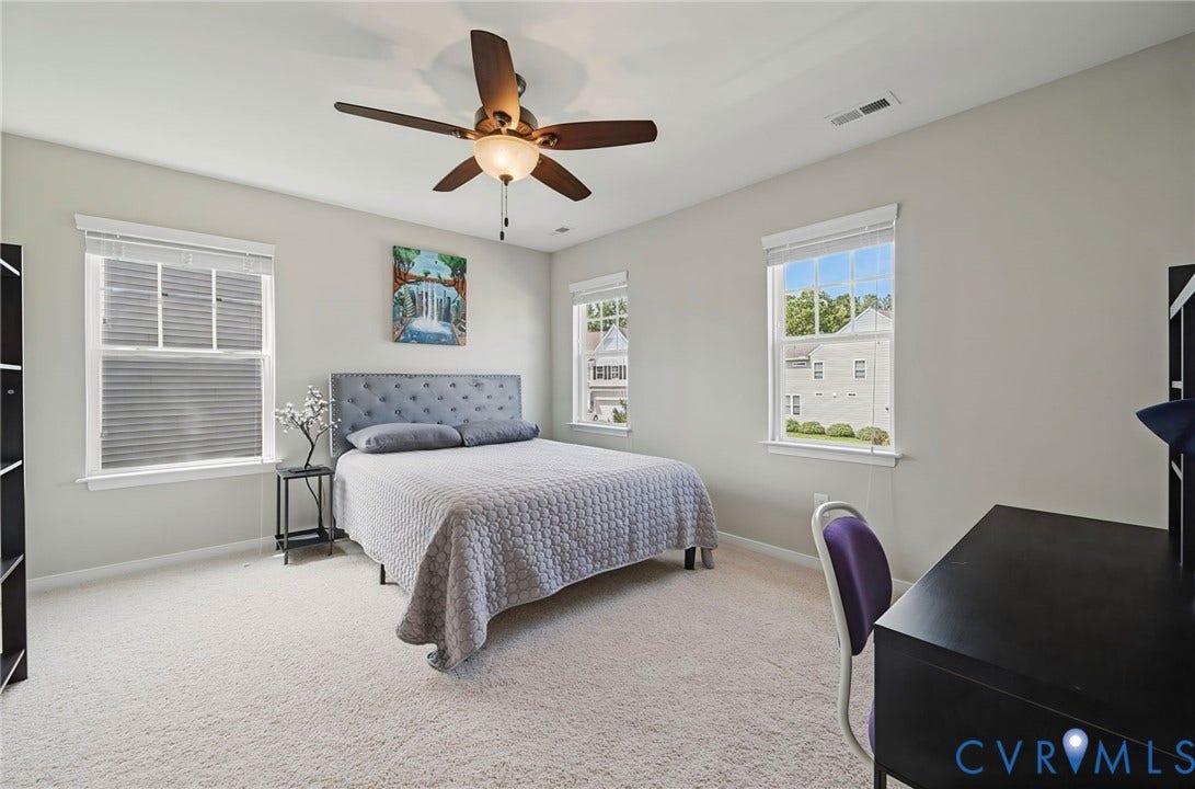 Bright room featuring neutral wall tones, multiple windows, a ceiling fan with integrated lighting, and soft carpeting