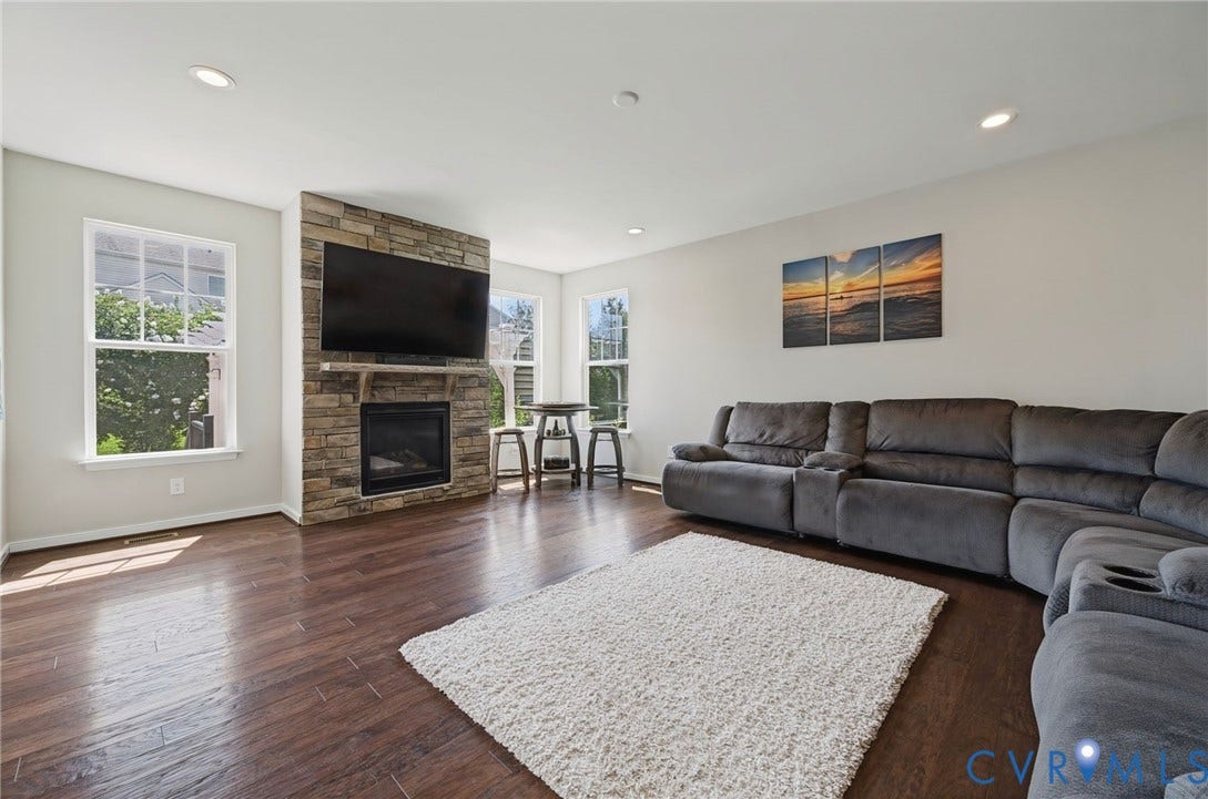 Stone-faced fireplace with a mantel, recessed lighting, wood-finish flooring, and multiple windows