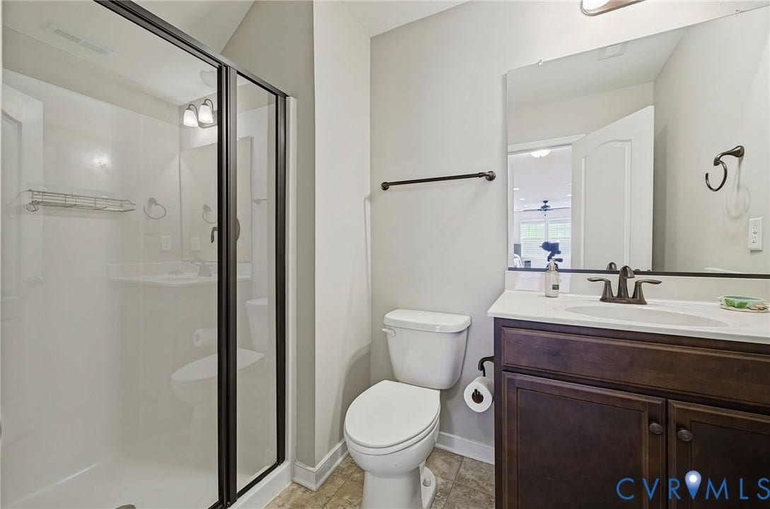 Walk-in shower with dark-framed glass enclosure, single vanity with dark wood-finish cabinetry, countertop, and a rectangular mirror