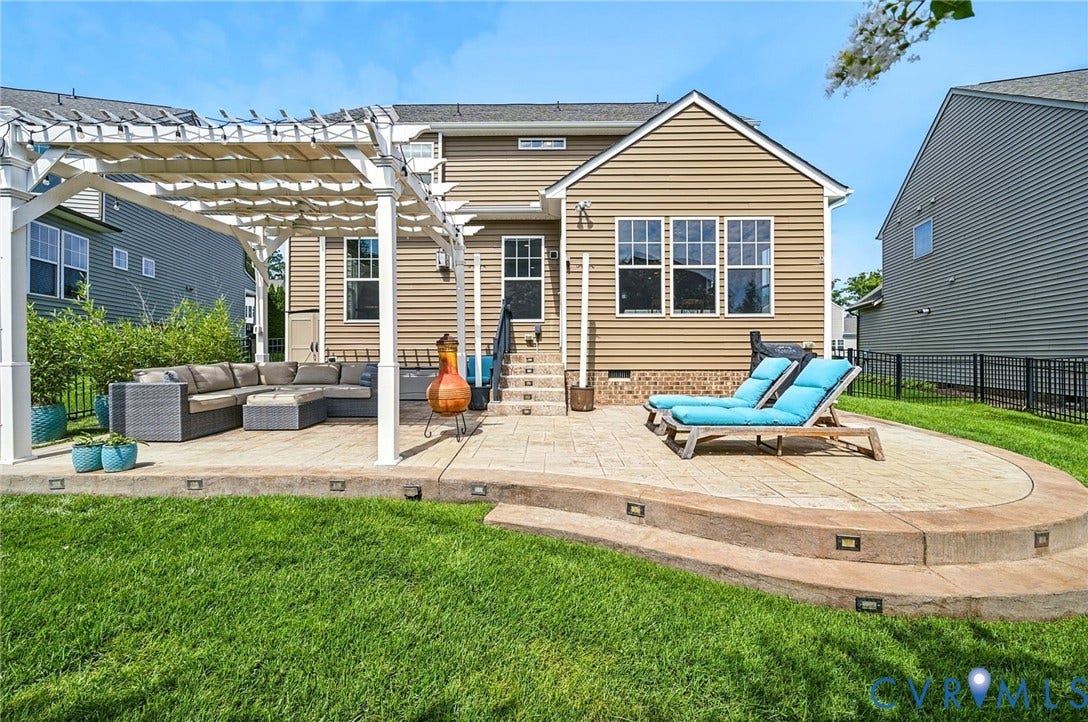 Expansive backyard featuring a multi-level stamped concrete patio, white pergola with retractable shade, and a green lawn area