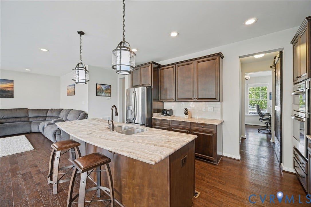 Kitchen island with a built-in sink, pendant lighting, hardwood flooring, dark wood-finish cabinetry, and stainless steel appliances