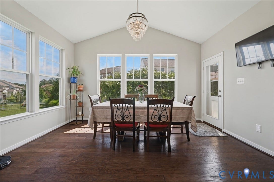 Vaulted ceiling with a crystal chandelier, multiple large windows, dark wood-finish flooring, and a glass-paneled door