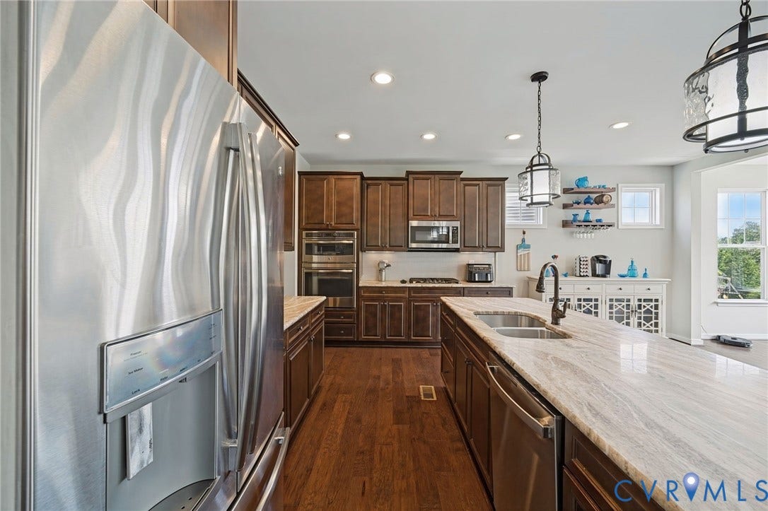 Spacious kitchen featuring wood-finish flooring, dark wood cabinetry, stainless steel appliances, a center island with an undermount sink, and recessed lighting