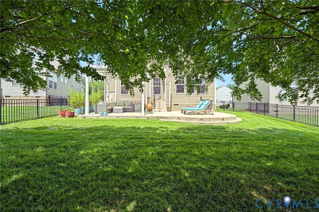 Expansive backyard featuring a manicured lawn, tiered concrete patio, and black metal fencing