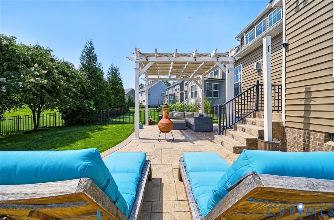 Expansive paver patio featuring a white pergola and a built-in outdoor staircase with black railings