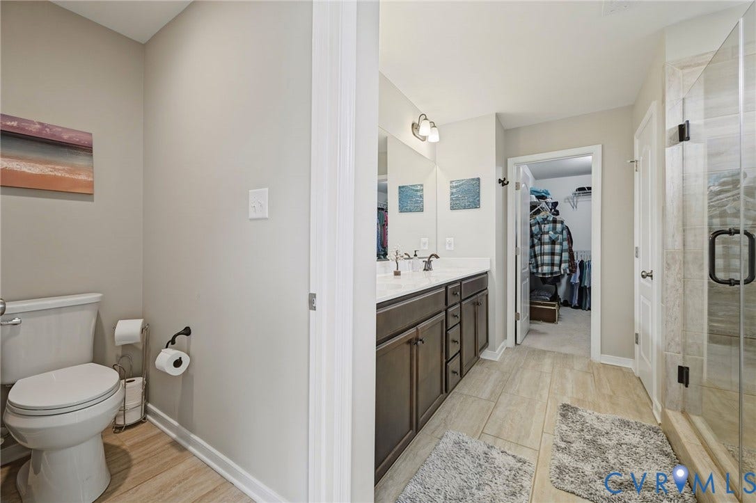 Dual vanity with dark wood-finish cabinetry, a large frameless mirror, and a full-size shower with a clear glass enclosure