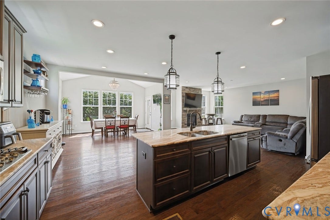 Expansive open-concept layout featuring rich wood-finish flooring, a kitchen island with integrated sink, and recessed lighting throughout
