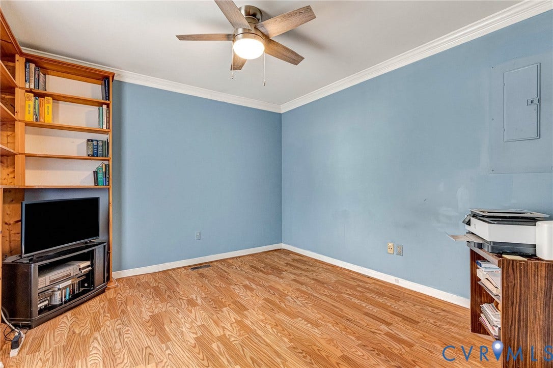 Wood-finish flooring, built-in shelving, ceiling fan with integrated lighting, and a white interior door