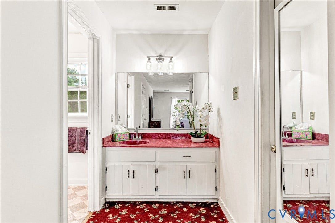 Vanity with a red basin sink and matching countertop, white cabinetry with silver hardware, and a wall-mounted mirror with a three-light fixture