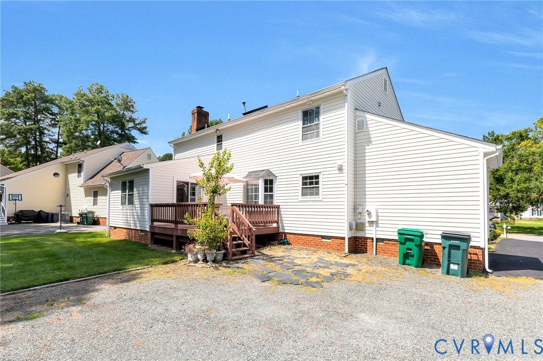 Expansive wood deck with stairs, white with siding, and a red brick foundation with a large private parking area