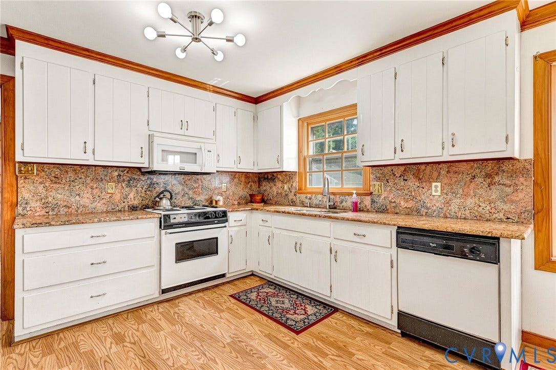 White cabinetry with ample storage, stone countertops, wood-finish flooring, built-in microwave, and a stainless steel sink with a window