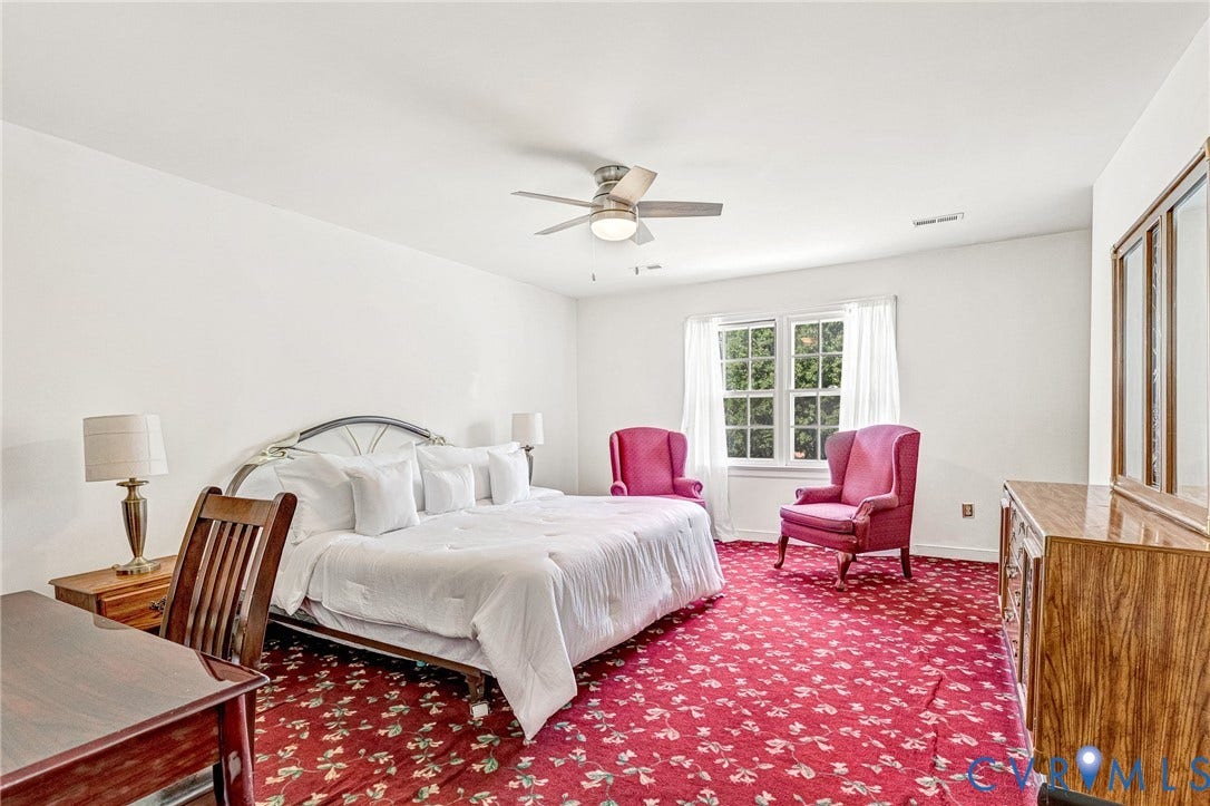 Spacious room featuring patterned carpeting, a multi-pane window, and a ceiling fan