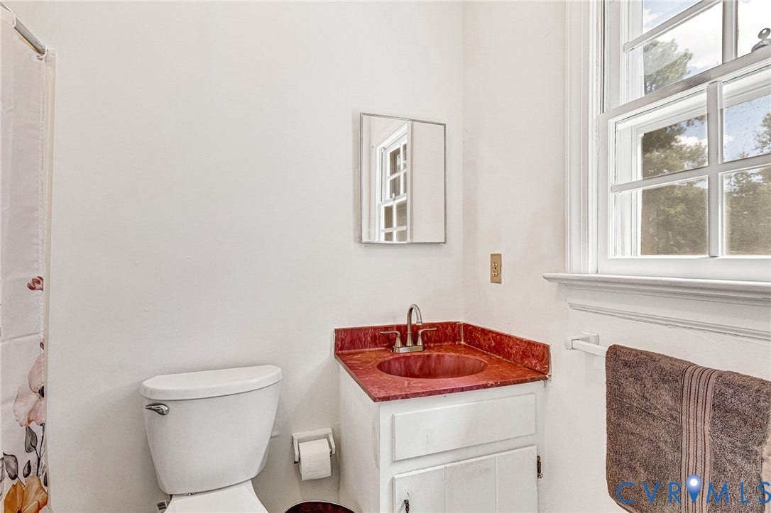 White vanity with red countertop and integrated sink, chrome faucet, white toilet, and a window with white trim