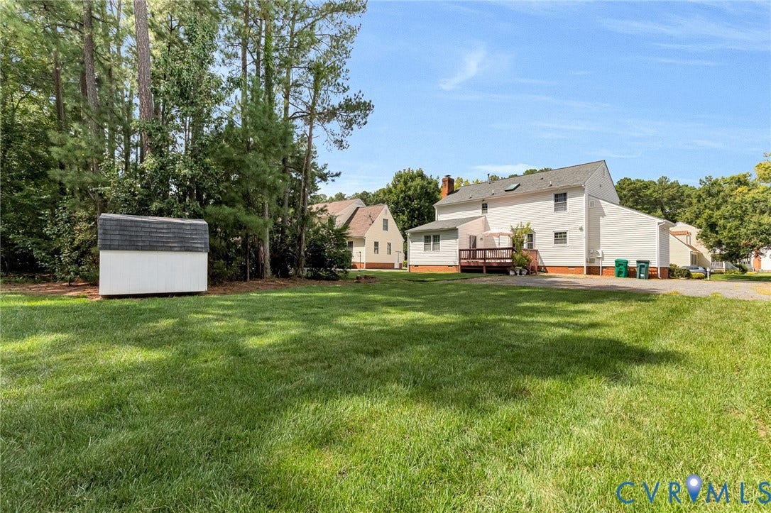 Expansive rear yard with a storage shed, wood deck, and mature trees