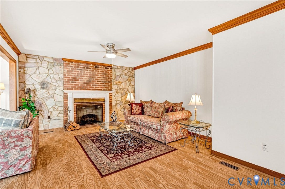 Wood-finish flooring, stone and brick fireplace with a white mantel, ceiling fan with integrated lighting, and wood trim accents