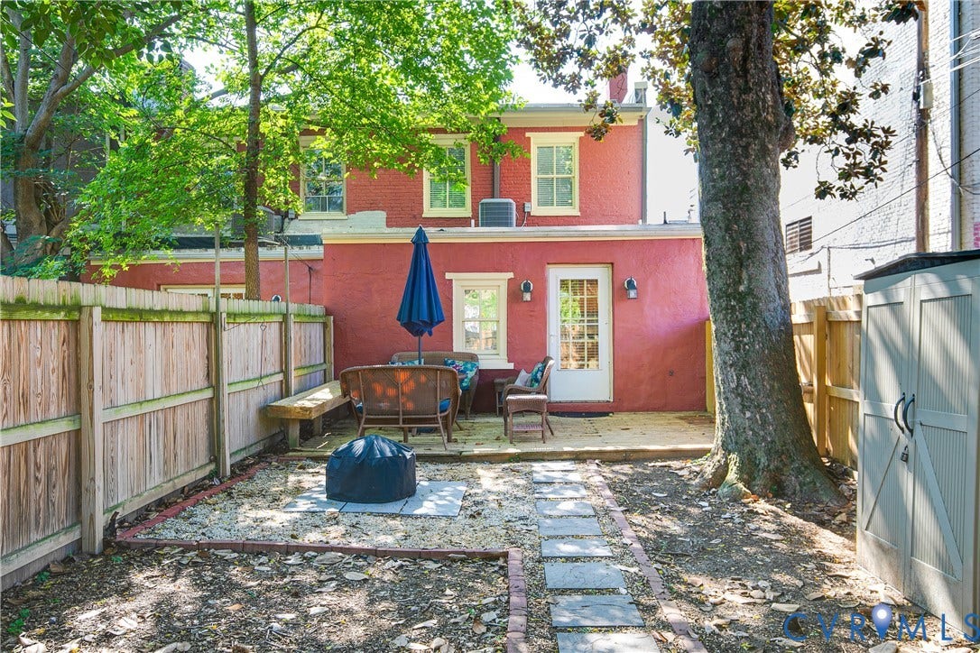 518 N 1st Street, Jackson Ward, Richmond, VA 23219 Charming brick exterior with mature shade trees and fenced backyard featuring stone pathway, patio seating area, and blue market umbrella
