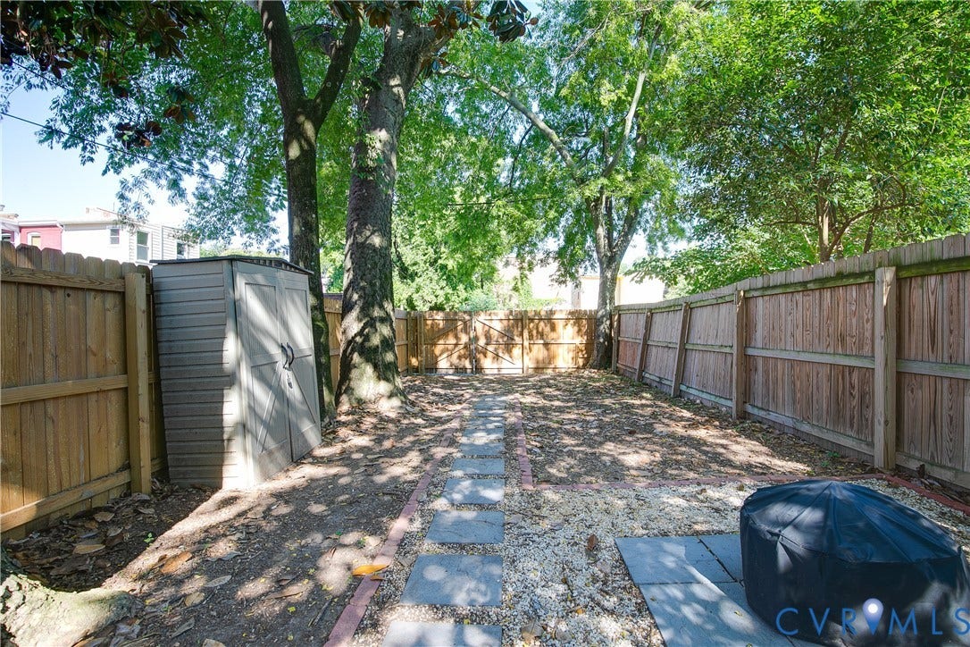 518 N 1st Street, Jackson Ward, Richmond, VA 23219 Mature shade trees frame this private side-yard passage, featuring wood-finish fencing on both sides, gravel hardscaping, and a detached storage structure