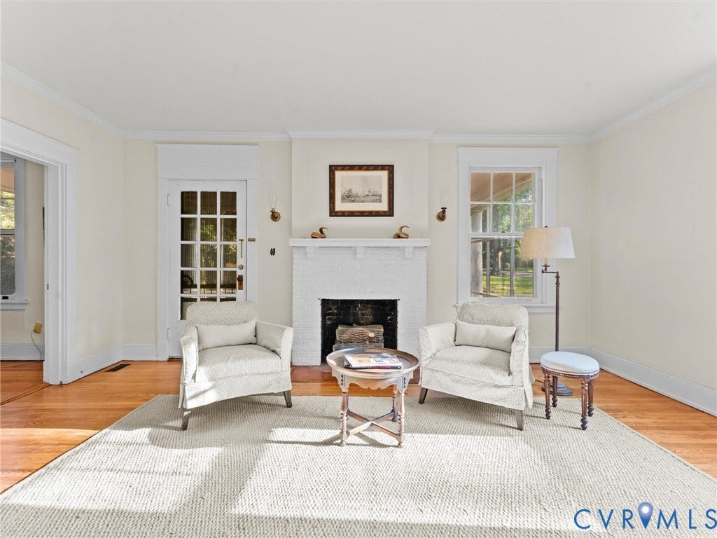 Hardwood flooring, white painted brick fireplace, crown molding, and a paneled glass door