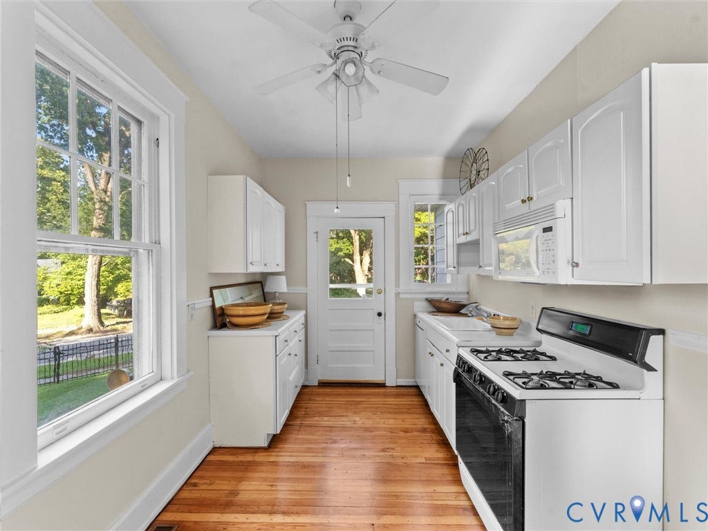 Galley kitchen featuring white cabinetry, wood-finish flooring, stainless steel gas cooktop, and large multi-pane windows overlooking the outdoor landscape