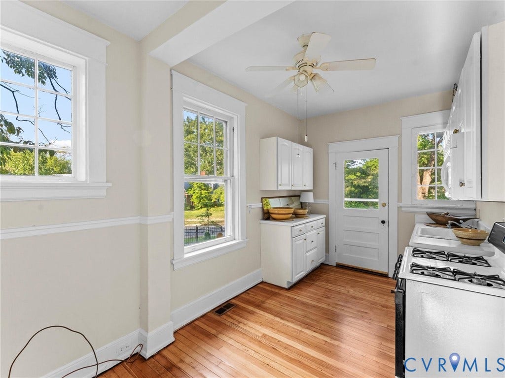 Bright and airy kitchen featuring white cabinetry, stainless steel appliances including a gas range and refrigerator, wood-finish flooring, and abundant natural light from multiple windows and glass doors