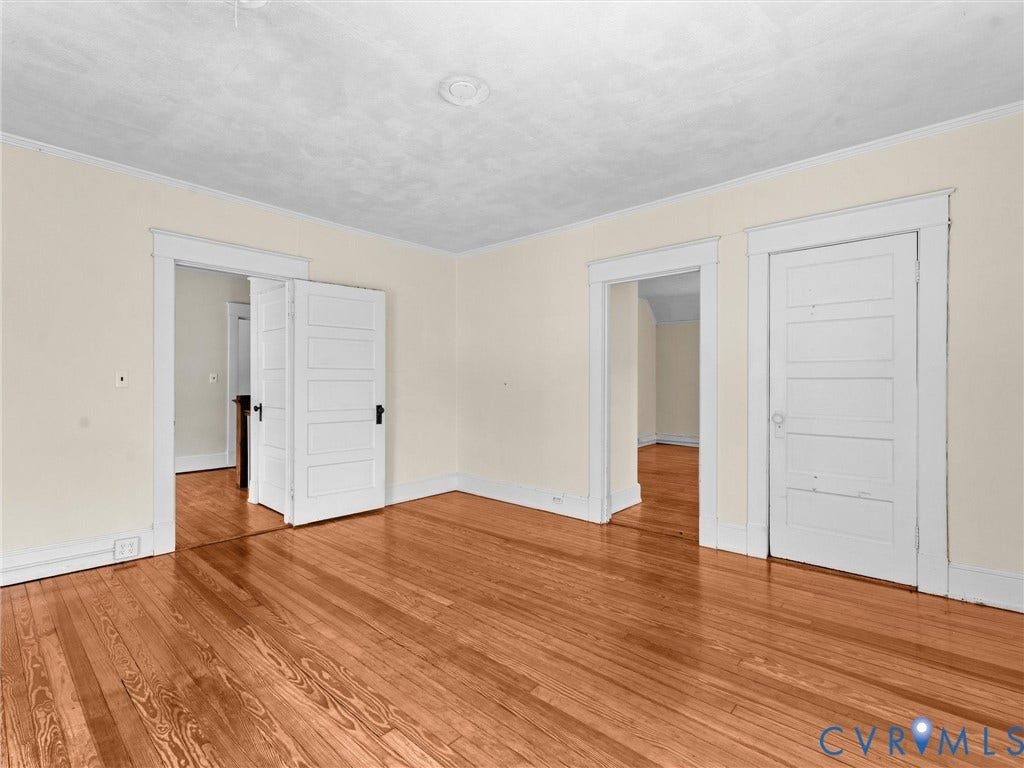 Spacious room featuring gleaming wood-finish flooring throughout, white six-panel closet doors, and multiple entry points