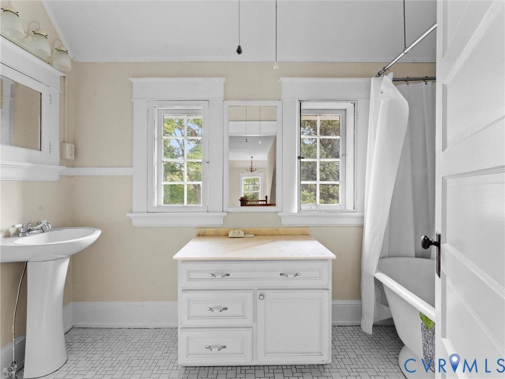Classic primary bathroom showcasing a white vanity with multiple drawers and chrome hardware, white subway tile wainscoting, pedestal sink, large mirror cabinet with integrated lighting, and hexagonal tile flooring
