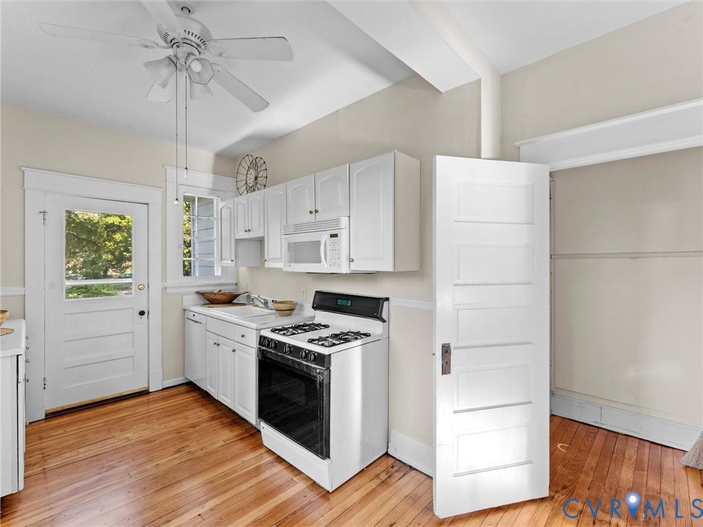 Bright, updated kitchen featuring white cabinetry, stainless steel gas range with black cooktop, white appliances, wood-finish flooring, and abundant natural light from exterior door and windows
