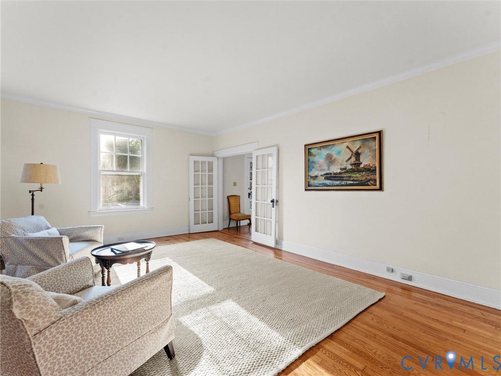 Spacious living room with hardwood flooring, abundant natural light from multiple windows, French doors opening to additional rooms, and neutral wall finishes throughout