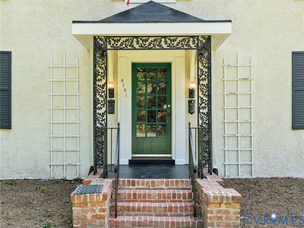 Elegant front entrance featuring a green paneled door with multi-pane glazing, ornate black and cream decorative surround, and a peaked roof overhang