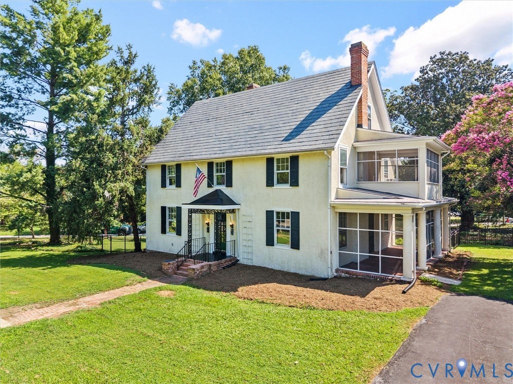 Classic Colonial residence featuring a cream-painted exterior with black shutters, a brick chimney, and a covered front portico with columns
