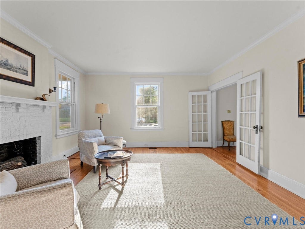 Bright, sun-filled living room showcasing hardwood flooring, a fireplace with white surround and mantel, and multiple windows providing natural light