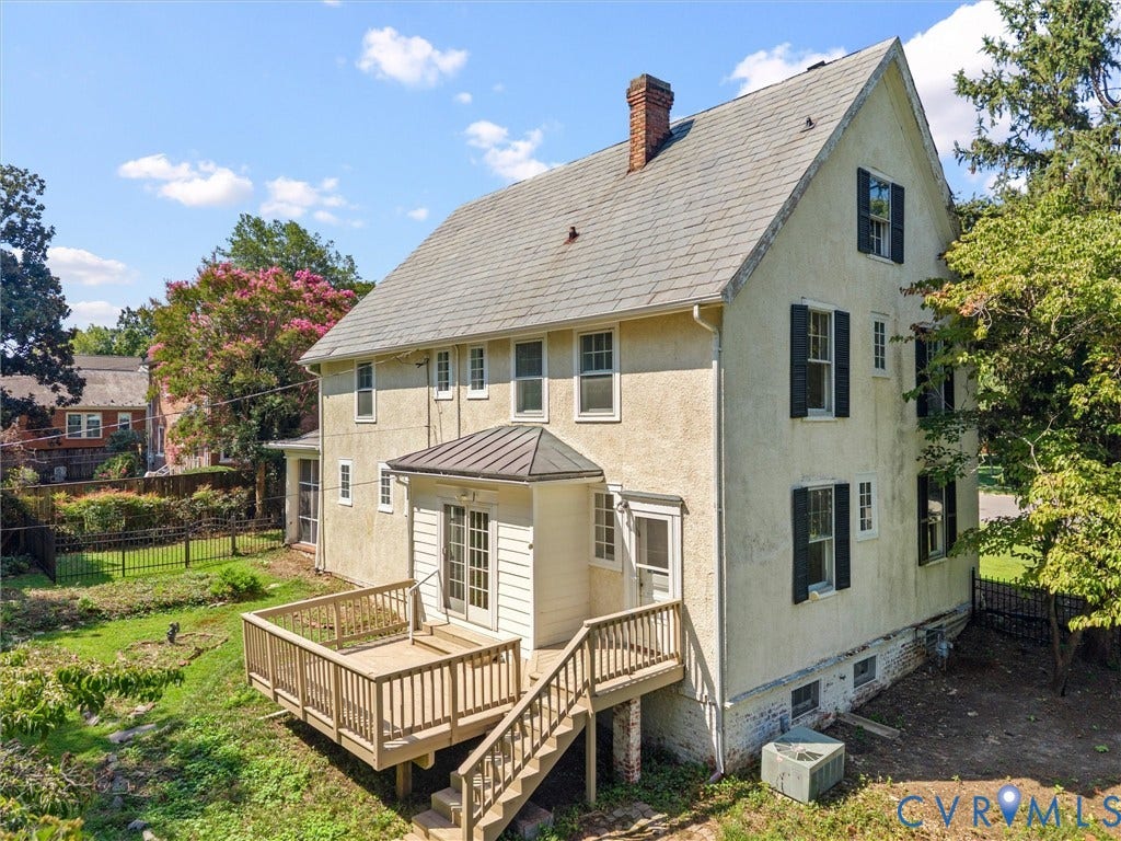 Charming Colonial-style residence featuring a cream-colored exterior with black-trimmed windows, steeply pitched roof with slate-gray shingles, and brick chimney