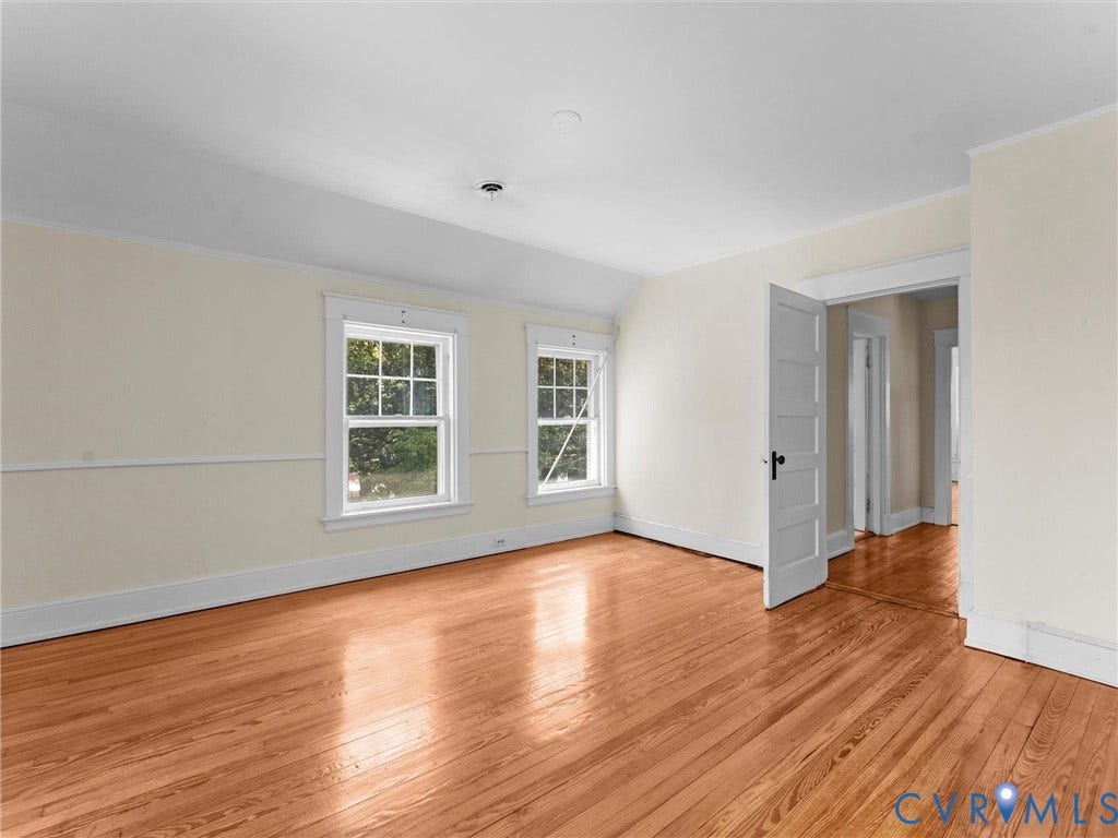 Bright, spacious room featuring gleaming wood-finish flooring, abundant natural light from dual double-hung windows with white trim, and clean white ceiling