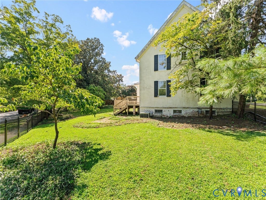 Charming two-story residence set on expansive grounds featuring mature shade trees, manicured lawn, and black metal fencing
